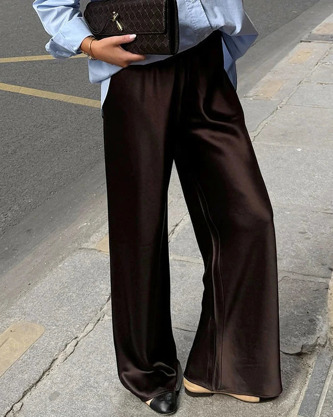 Person wearing brown wide-leg pants and holding a brown handbag on a street.